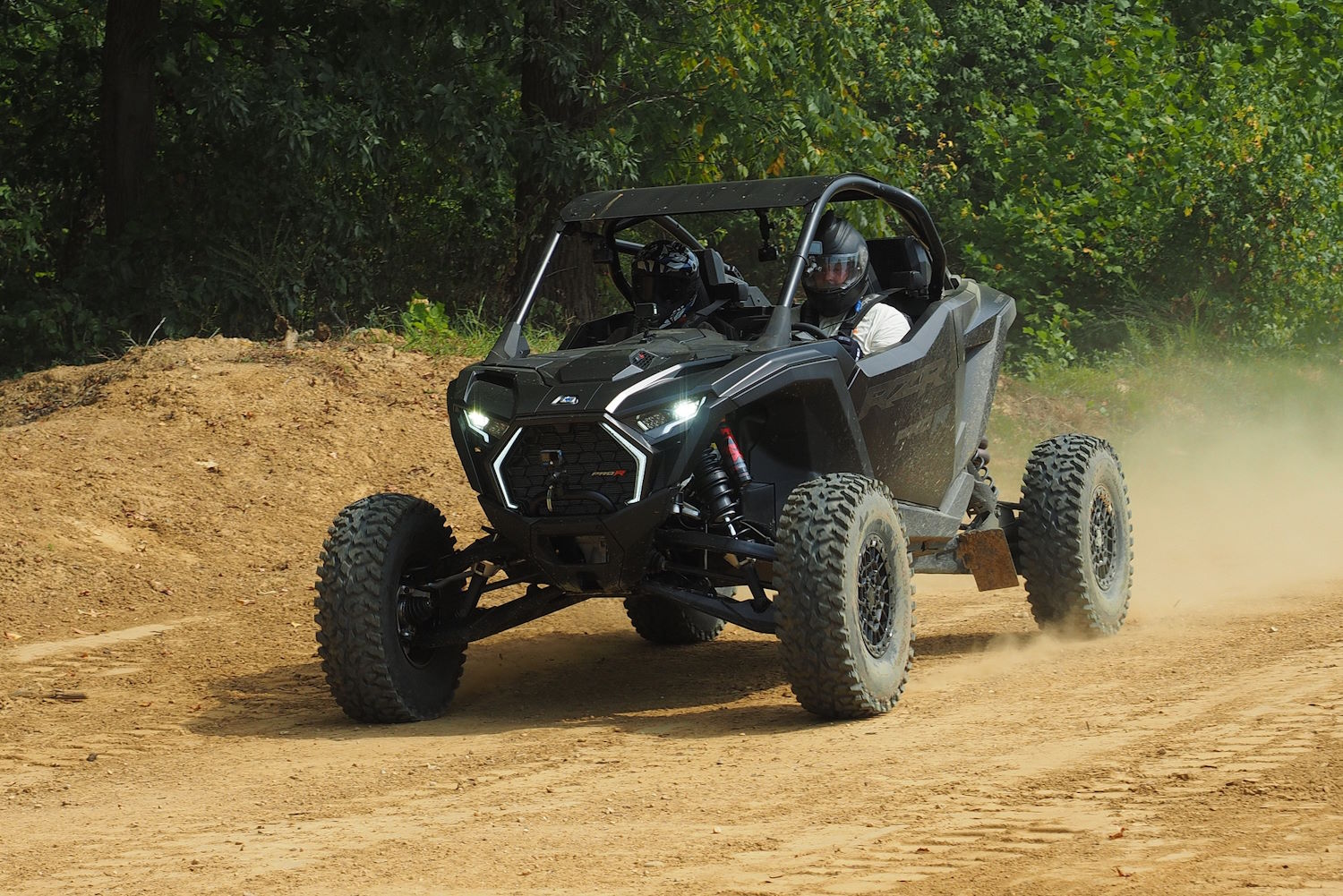 Two riders driving a 2025 Polaris RZR Pro R off-road vehicle on a dirt trail